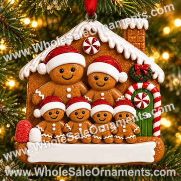 Gingerbread family of six Christmas ornament beside a candy-trimmed gingerbread house and blank plaque, hanging on a Christmas tree with warm lights
